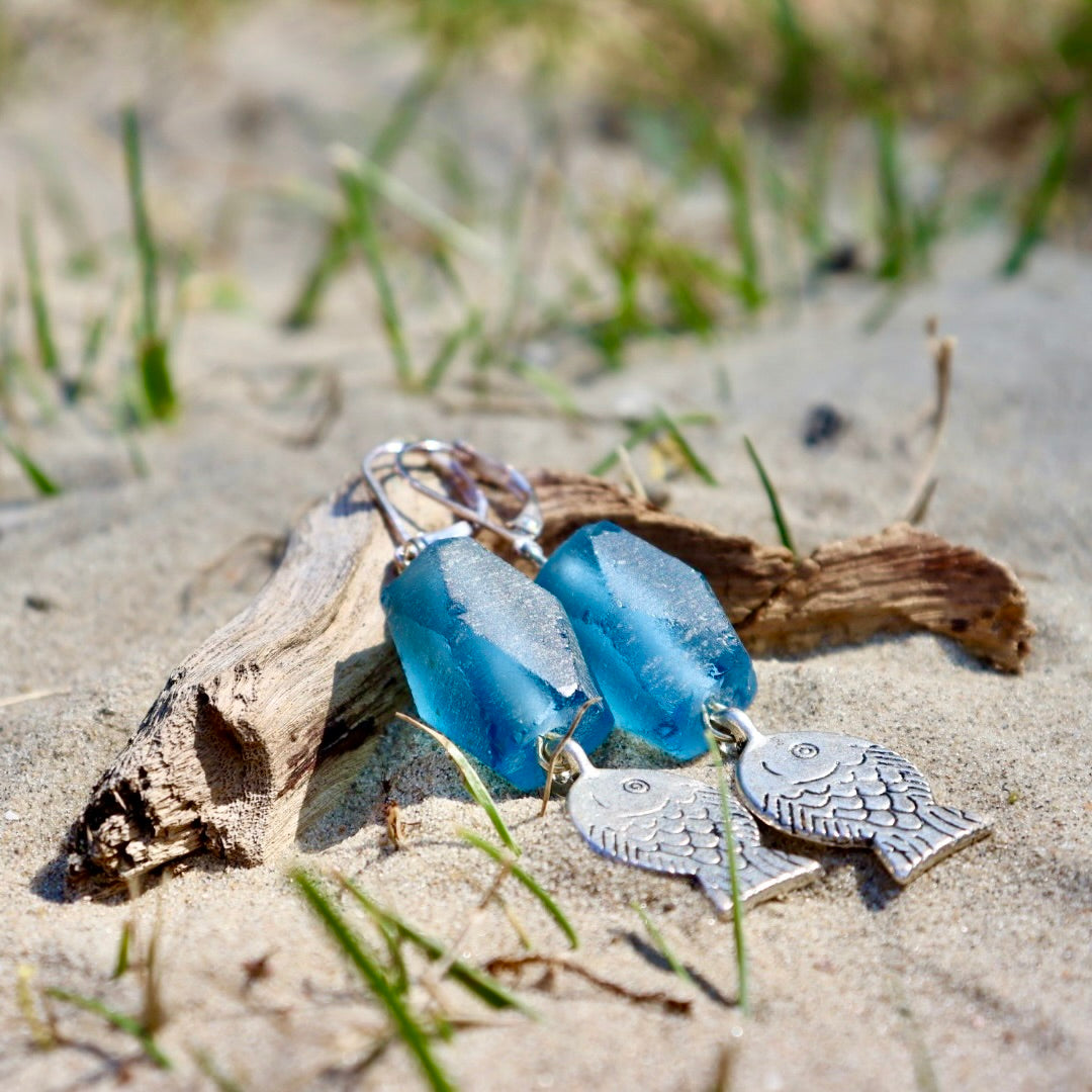 Marotta collectie Ocean blue Gemma- gemdroom - oorbellen. bestaande uit een murano glas in facet rondom afgewerkt. een oceaan blauwe kleur. Afgewerkt met een zilveren visje onderaan de hanger. foto getrokken op het strand met watereffect. creool als slot. De winkel voor jou handgemaakte juwelen, keramiek kaarsen en edelstenen.